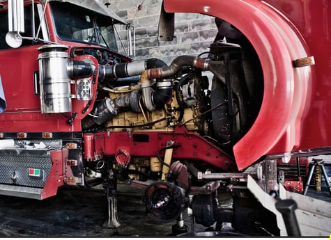 a close-up of a red heavy-duty truck with its hood open, showing the engine and mechanical components